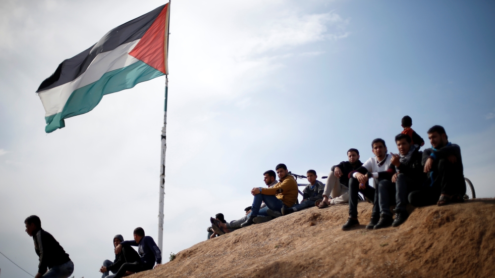 Palestinian sit near to the Israeli-Gaza border fence, ahead of the first anniversary of border protests, east of Gaza City