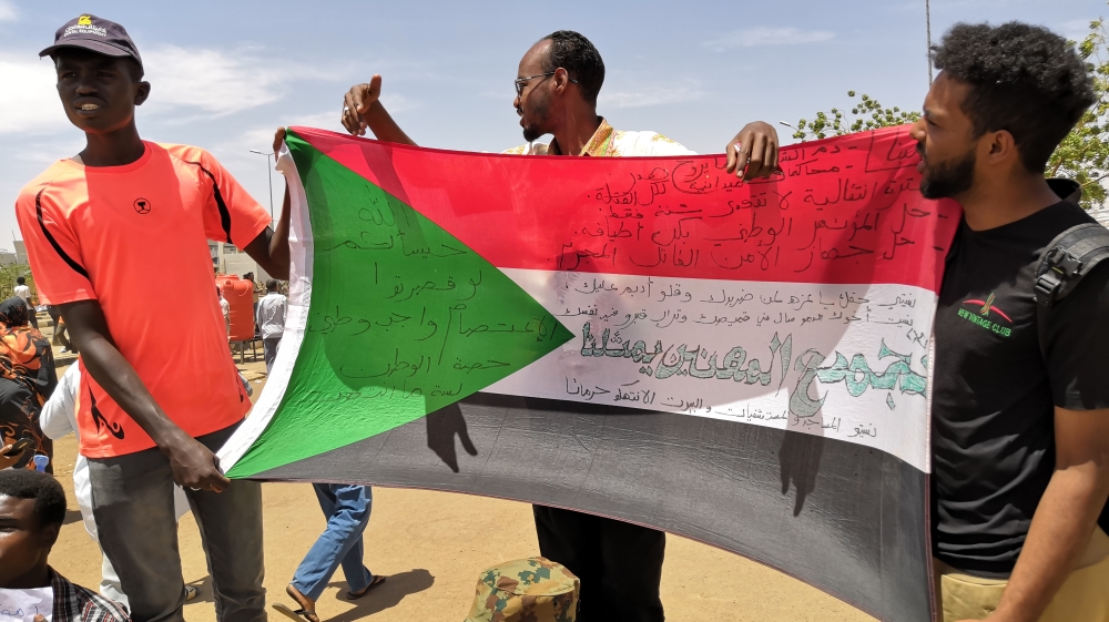 Young Sudanese carry a national flag as they rally in the capital Khartoum [Ashraf Shazly/AFP]
