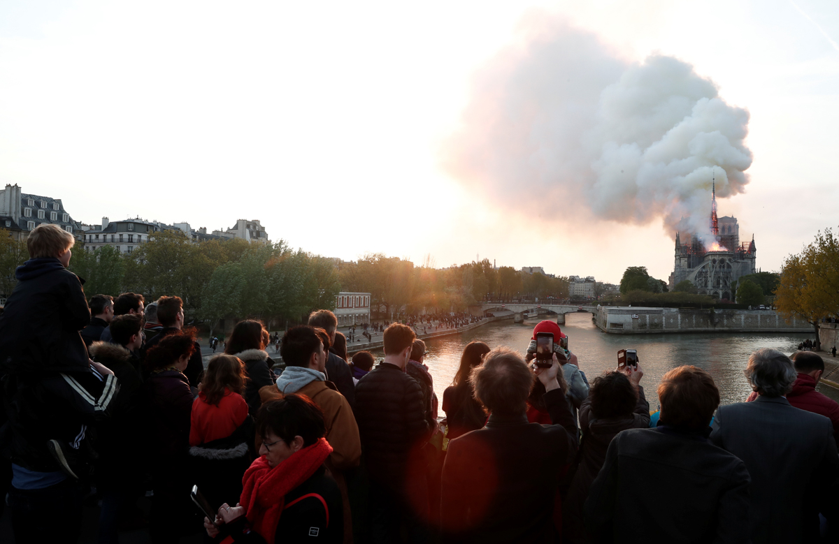 People watch from a bridge as smoke billows from Notre Dame Cathedral during a fire in Paris, France April 15, 2019. REUTERS/Benoit Tessier -