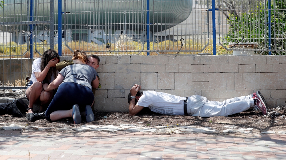 Israelis take cover as they hear sirens warning of incoming rockets from Gaza, during cross-border hostilities, in the southern Israeli city of Ashkelon [Ronen Zvulun/Reuters]