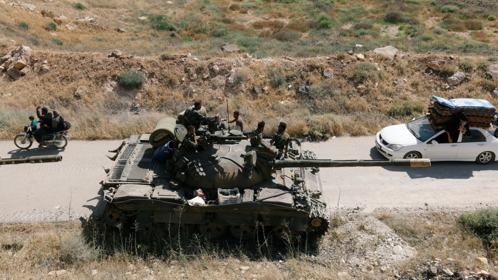 Civilians pass by a Syrian forces'' tank of President Bashar al Assad in Deraa