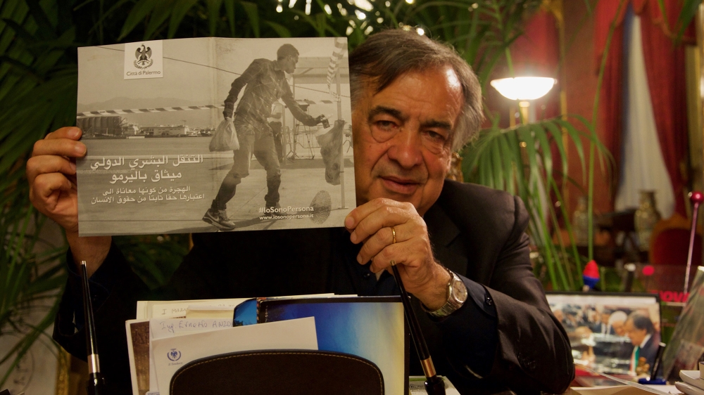 Palermo Mayor Leoluca Orlando holds up a pamphlet on migrant rights in his office in city hall [Savin Mattozzi/Al Jazeera]