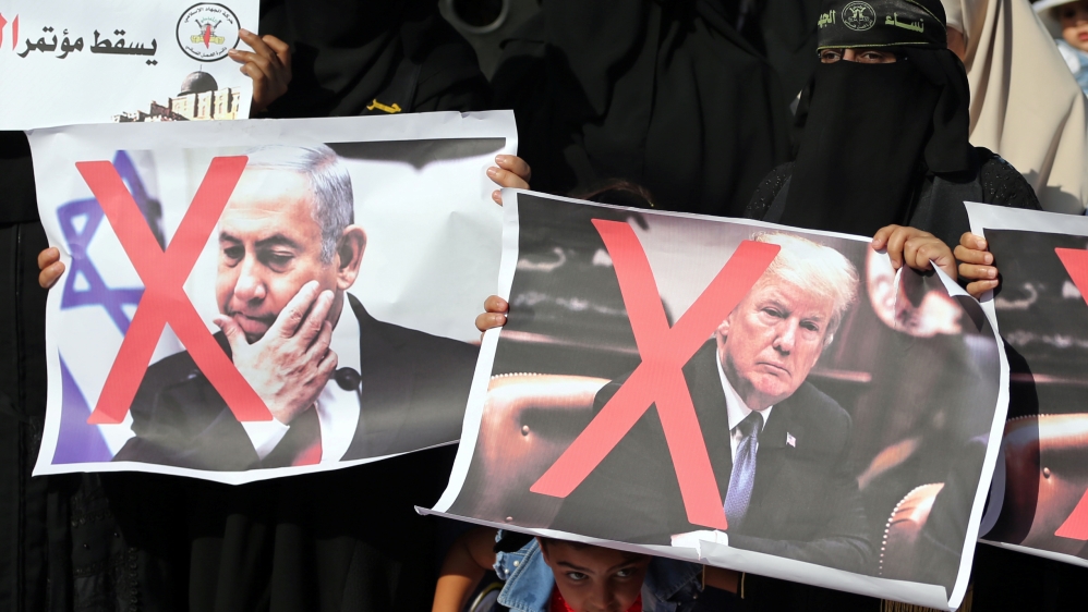 Girl looks on as Palestinian women hold crossed-out posters depicting Trump and Netanyahu during a protest against Bahrain''s workshop for U.S. peace plan, in the southern Gaza Strip