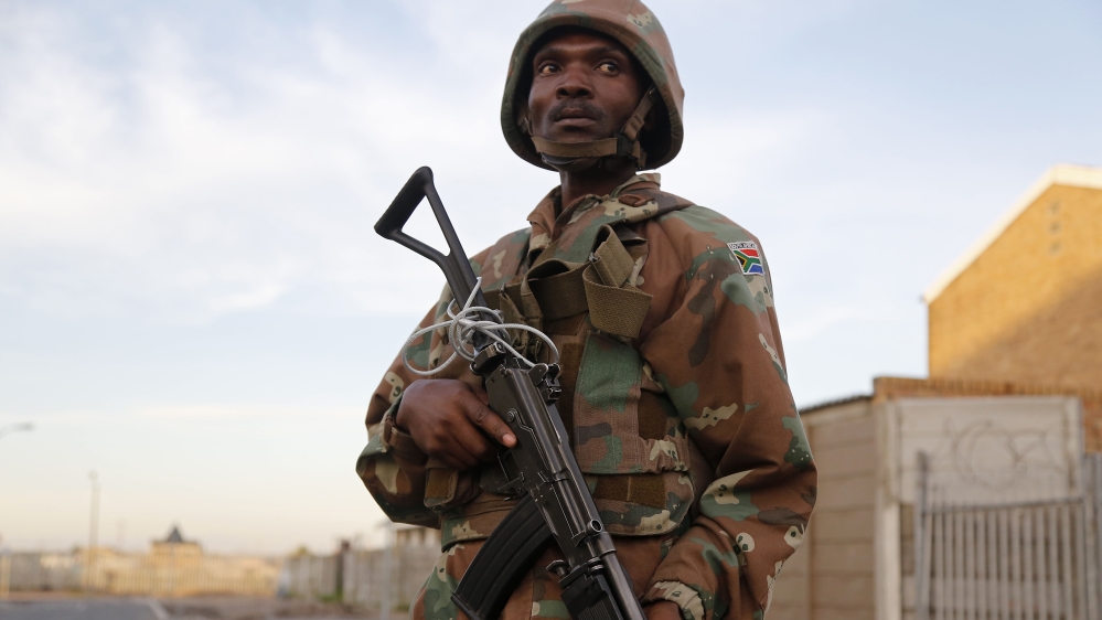 A South African soldier provide security for policemen as they look for drugs in Manenberg, South Africa, Thursday, May 21, 2015