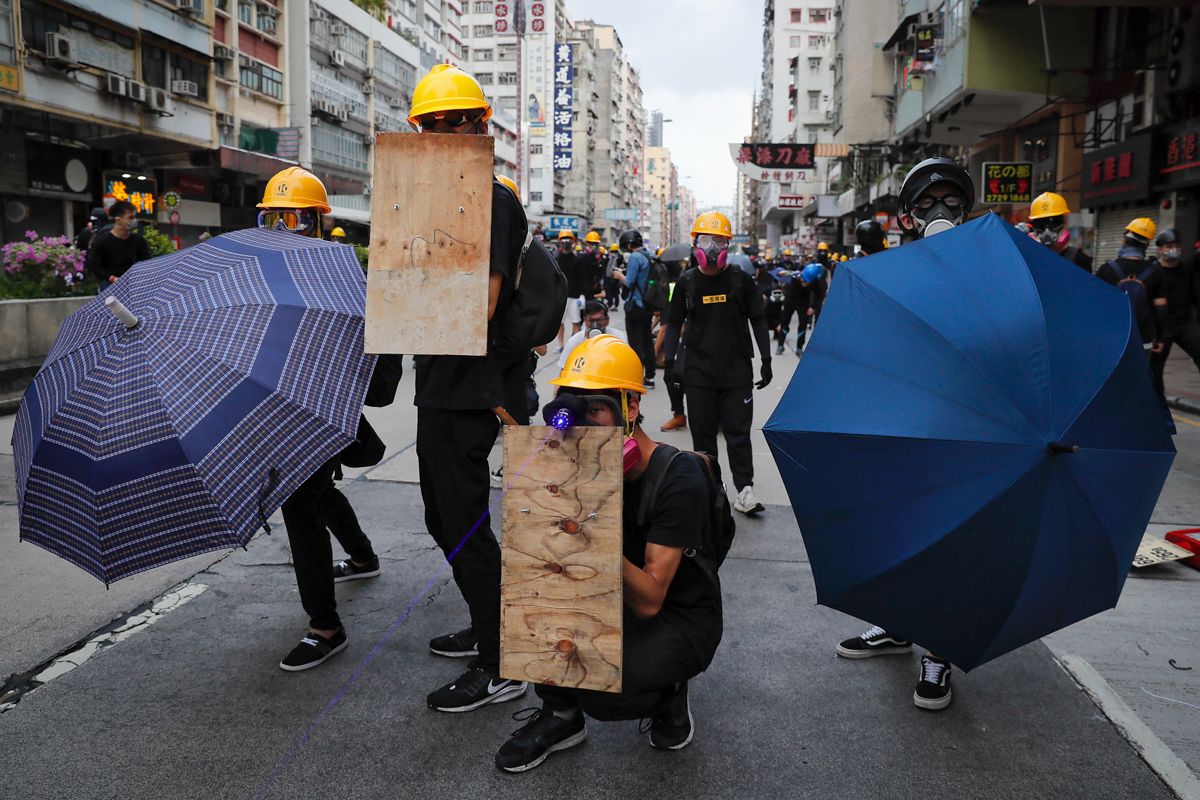 Protesters with umbrellas and homemade shields as they face with riot policemen on a street in Hong Kong, Sunday, Aug. 11, 2019. Police fired tear gas late Sunday afternoon to try to disperse a demons