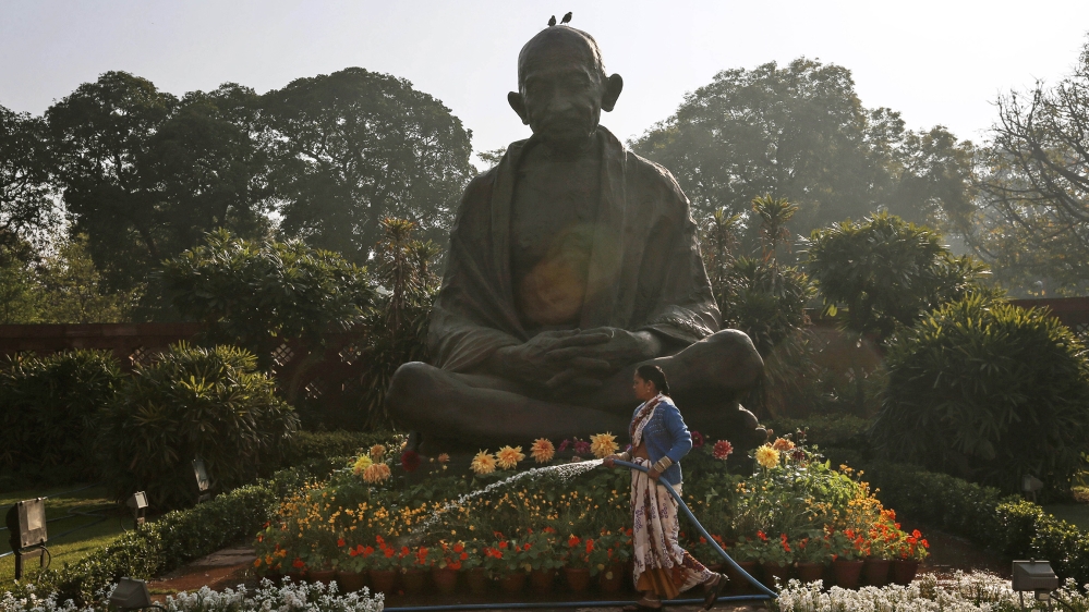 A worker waters plants around a statue of Mahatma Gandhi in New Delhi, India