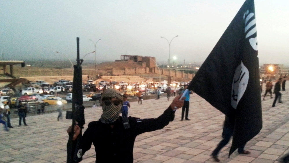 A fighter of ISIL holds a flag and a weapon on a street in Mosul