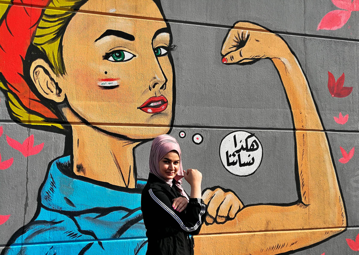 A woman poses for a picture near a graffiti with Arabic reading "those are our women" during ongoing protests near Tahrir Square in Baghdad, Iraq, Thursday, Nov. 7, 2019. (AP Photo/Khalid Mohammed)