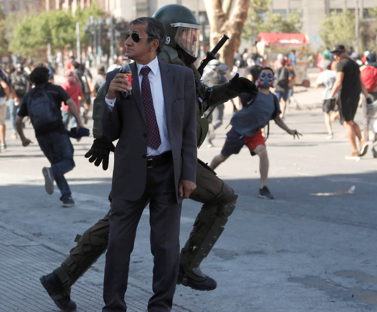 A man drinks a Frucola as a policeman chases demonstrators during a protest against Chile''s government in Santiago, Chile December 4, 2019. REUTERS/Goran Tomasevic REFILE - CORRECTING BEVERAGE''S NAME