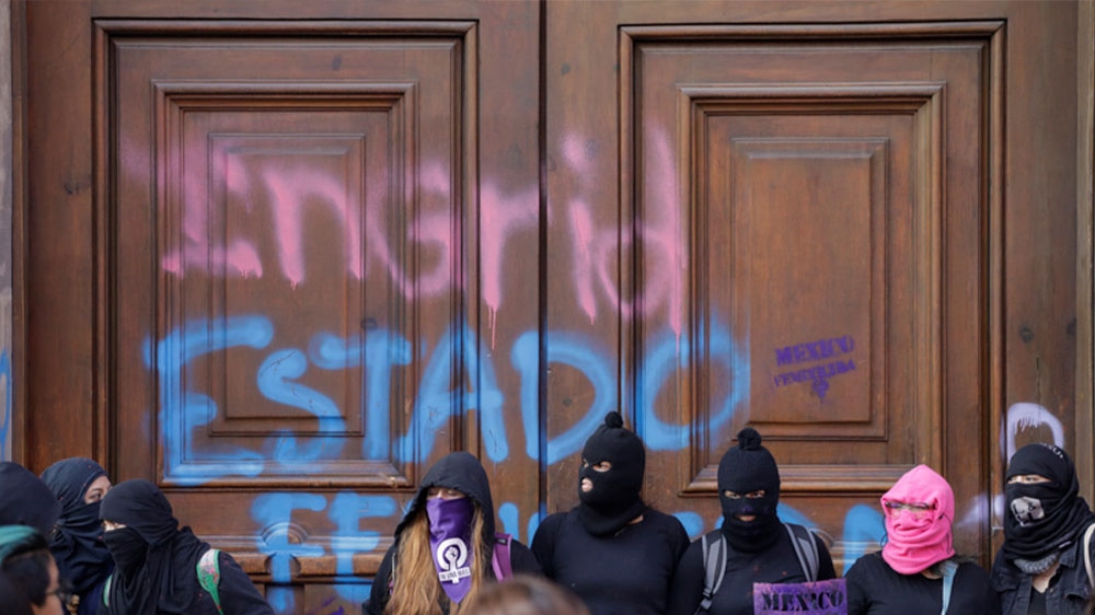 Demonstrators standing in front of presidential palace doors with words reading, ‘Ingrid’ and ‘femicide state’ in downtown Mexico City