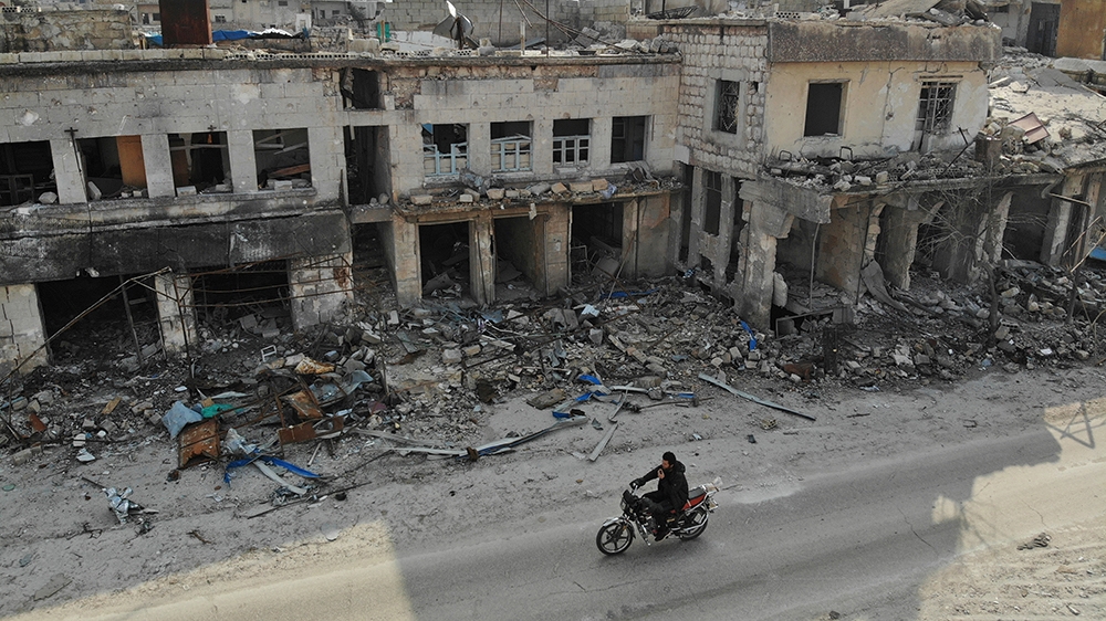 An aerial view taken on February 19, 2020 shows a man riding his motorcycle past destroyed buildings in the Syrian town of Ihsim in the southern countryside of Idlib. (Photo by Omar HAJ KADOUR / AFP)