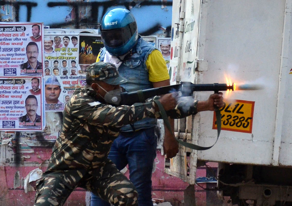 A police officer fires a tear gas shell to disperse crowds after a clash between people supporting a new citizenship law and those opposing the law, in Maujpur area of New Delhi, India, February 23, 2