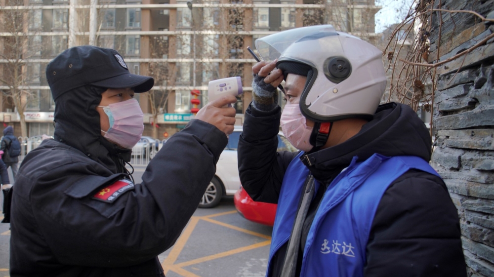 A security officer measures the temperature of a delivery worker at a residential compound in Beijing