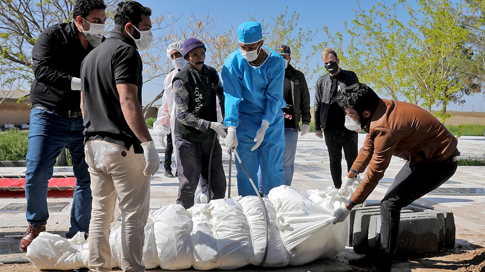 People wearing protective clothing, masks and gloves, attend a funeral of a victim who died after being infected with the new coronavirus, at a cemetery just outside Tehran, Iran, Monday, March 30, 20