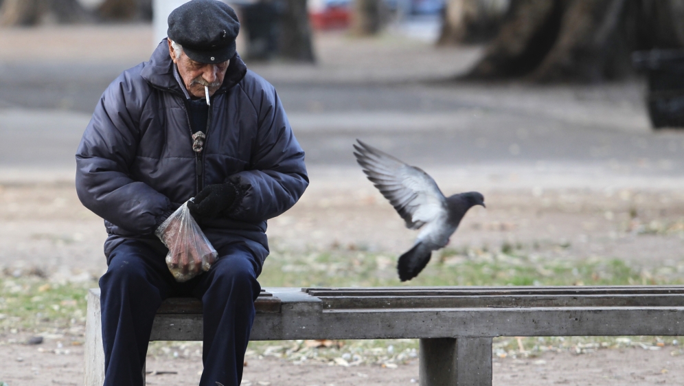 A retired man feeds pigeons at a public park in Buenos Aires
