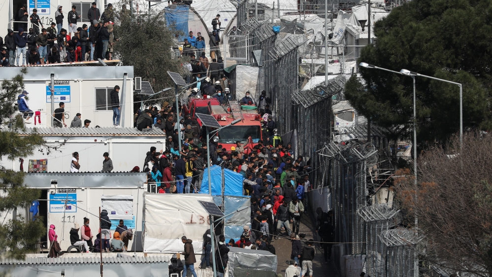 Refugees and migrants gather around a firefighting vehicle as a fire burns containers used as shelter in the Moria camp on the island of Lesbos