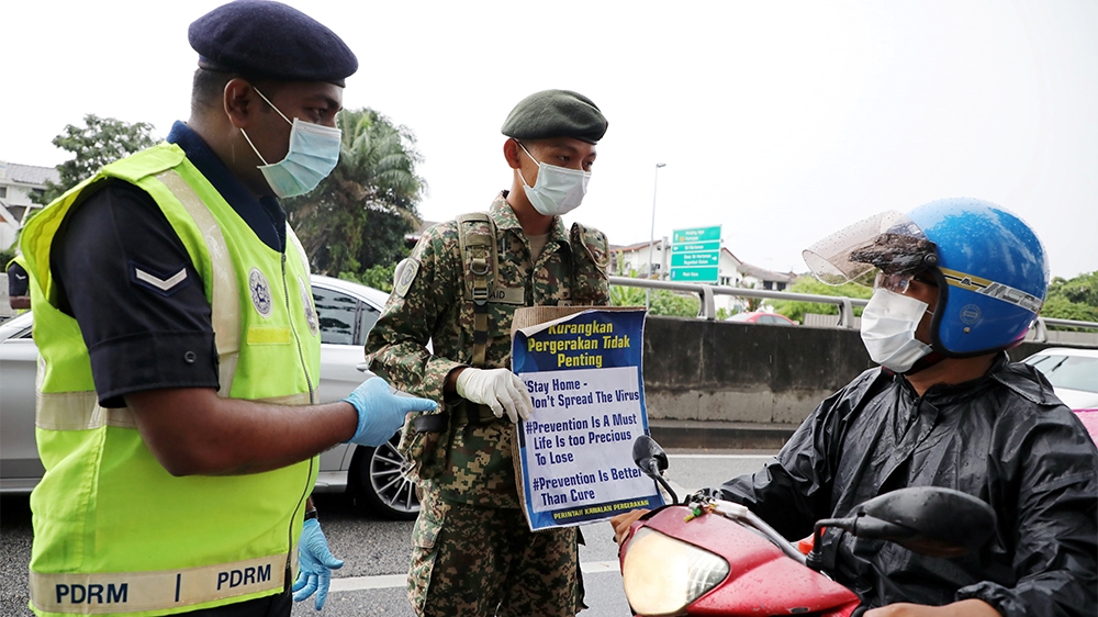 A soldier and a police officer wearing protective masks show a placard to a motorcyclist at a roadblock set up to enforce movement control order due to the outbreak of the coronavirus disease (COVID-1