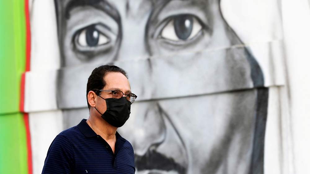 FILE PHOTO: A Saudi man walks past a poster depicting Saudi King Salman bin Abdulaziz, after a curfew was imposed to prevent the spread of the coronavirus disease (COVID-19), in Riyadh, Saudi Arabia M