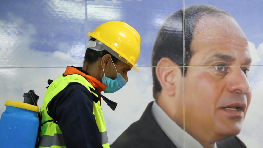 A member of medical team is seen beside a banner for the Egyptian President Abdel Fattah el-Sisi, as he sprays disinfectant at the Al Shohadaa "Martyrs" metro station in Cairo