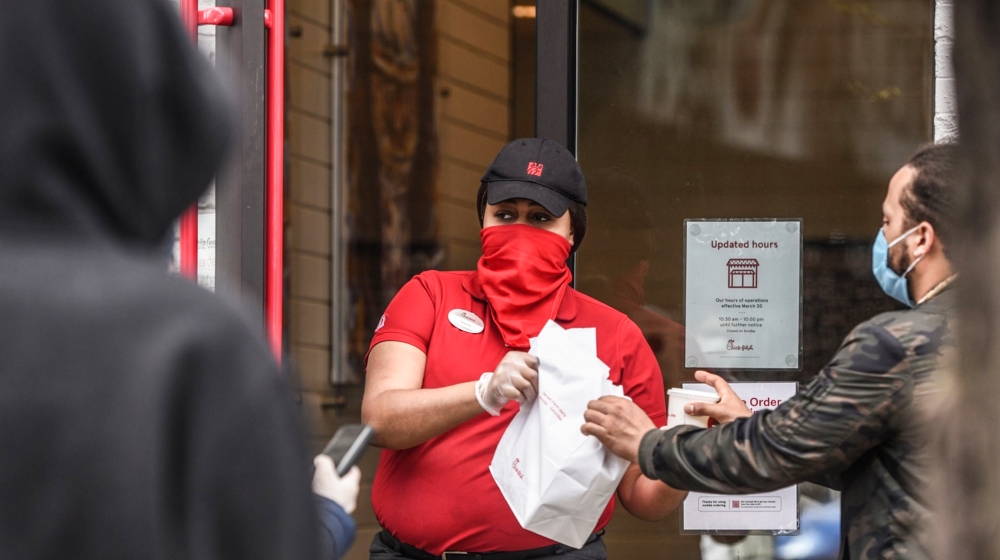 An employee wearing a protective mask and gloves hands out takeout orders to customers outside a Chick-fil-A Inc. restaurant in the Brooklyn Borough of New York, U.S., on Wednesday, April 15, 2020. Ne