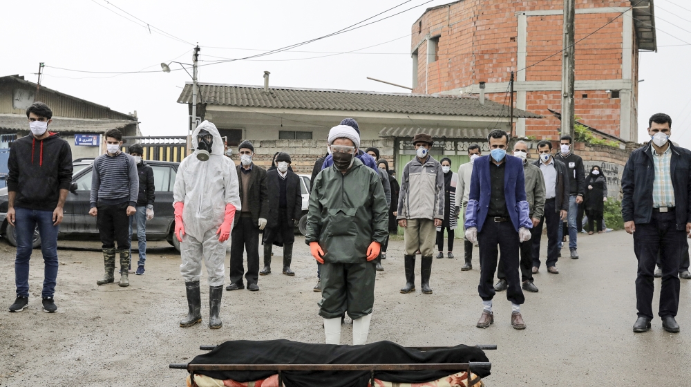 Mourners wearing protective clothing, face masks and gloves, pray over the body of a victim who died after being infected with the new coronavirus, in the outskirts of the city of Babol, in north of I