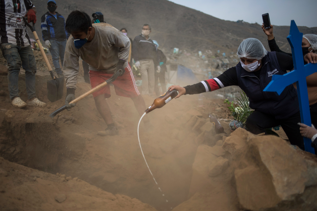 Relatives pour beer into the tomb of Victor Gaspar, who died of COVID-19 complications, during his burial at the Nueva Esperanza cemetery on the outskirts of Lima, Peru, Thursday, May 28, 2020. (AP Ph