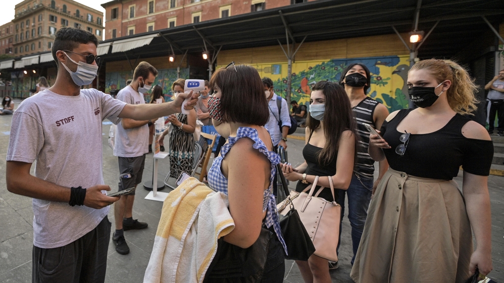 A worker wearing a face mask (L) checks the body temperatures of moviegoers to screen for possible infections with the SARS-CoV-2 coronavirus that causes the pandemic COVID-19 disease on the opening n