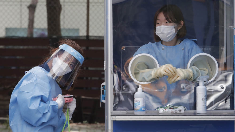 A medical worker holds a portable fan during the sweltering heat while police officers are tested for COVID-19 at a makeshift clinic at the Seoul Metropolitan Police Agency in Seoul, South Korea, Wedn