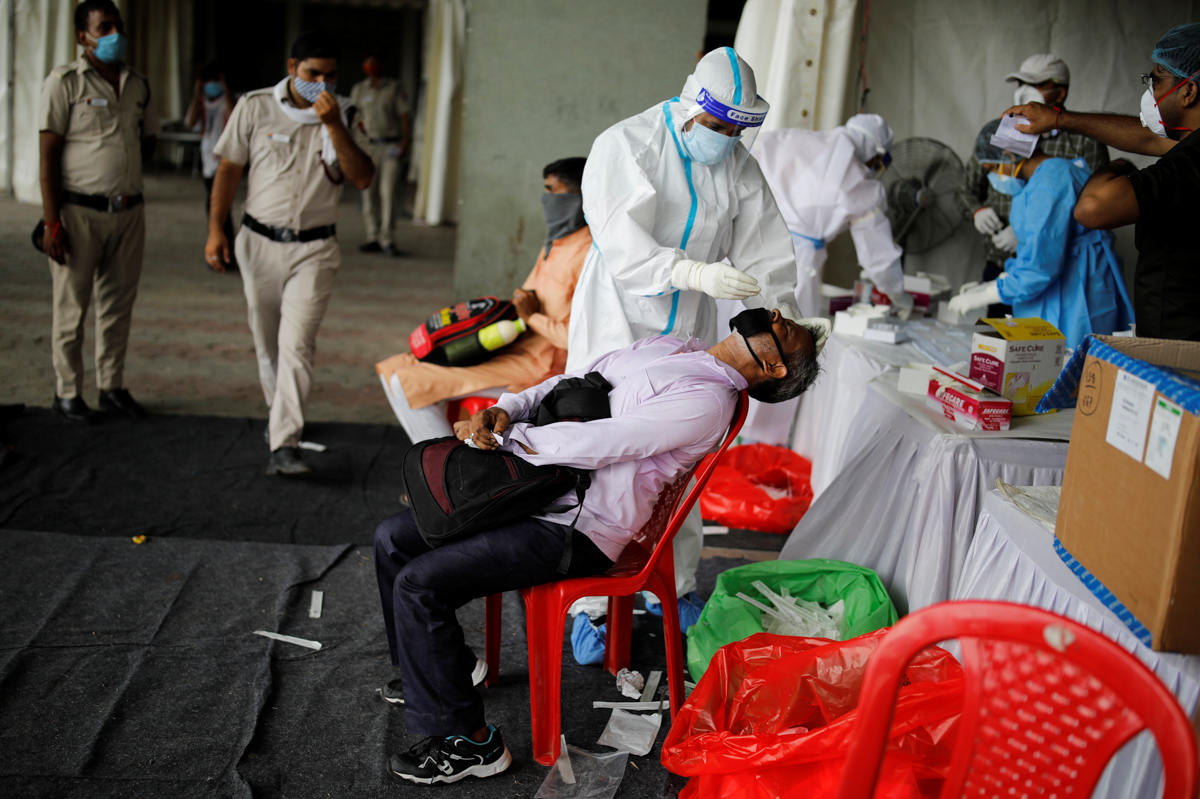 A healthcare worker wearing personal protective equipment (PPE) takes a swab from a migrant worker, who returned to Delhi from his native state, for a rapid antigen test at a bus terminal, amidst the