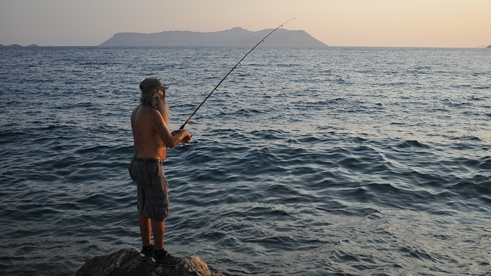 Man fishes in Kas, with Meis in background [Samuel Kent/Al Jazeera]