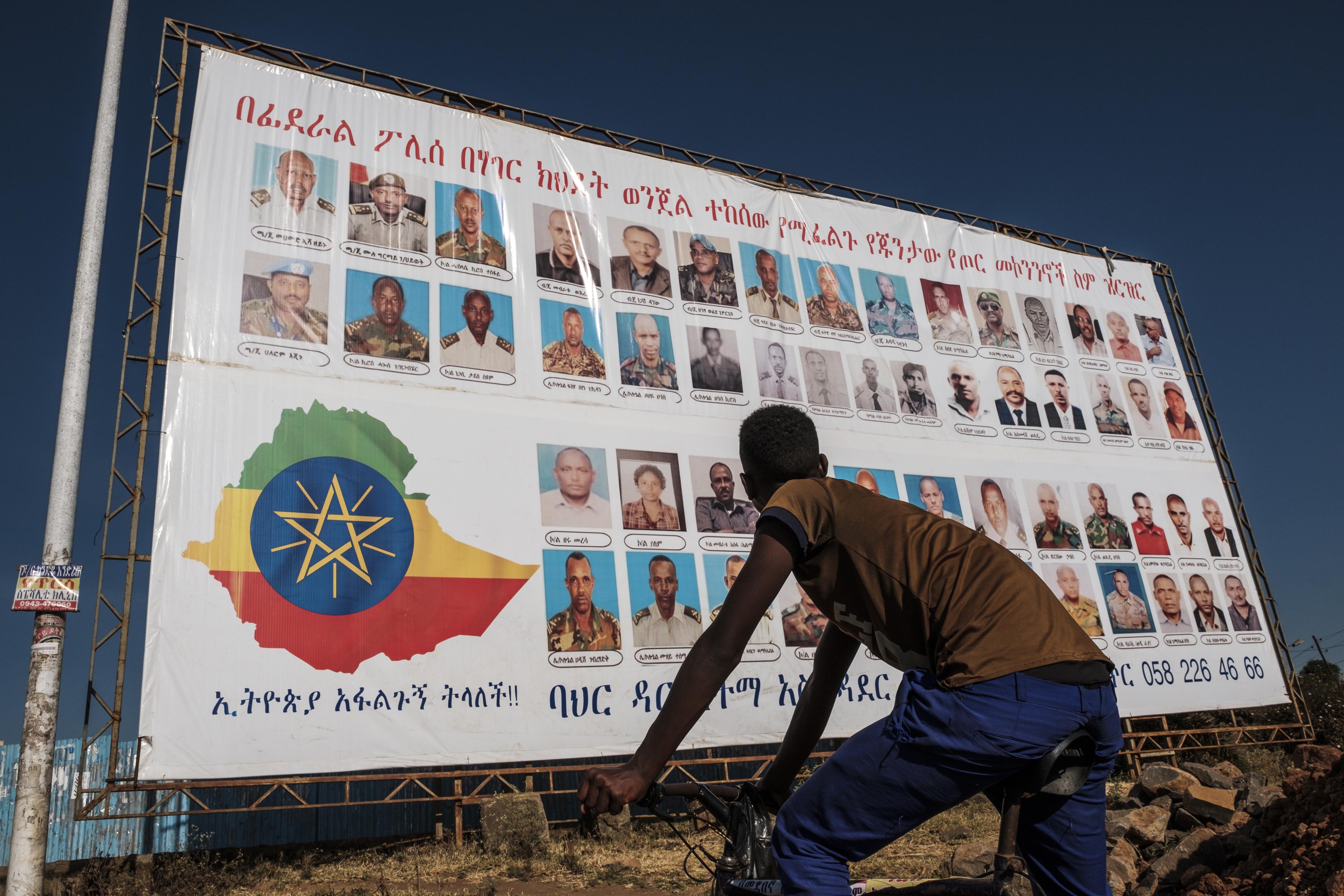 A youngster stands in front of a sign that depicts TPLF members as wanted by the Ethiopian federal police in Bahir Dar, Ethiopia, on November 26, 2020 [File: Eduardo Soteras/AFP]