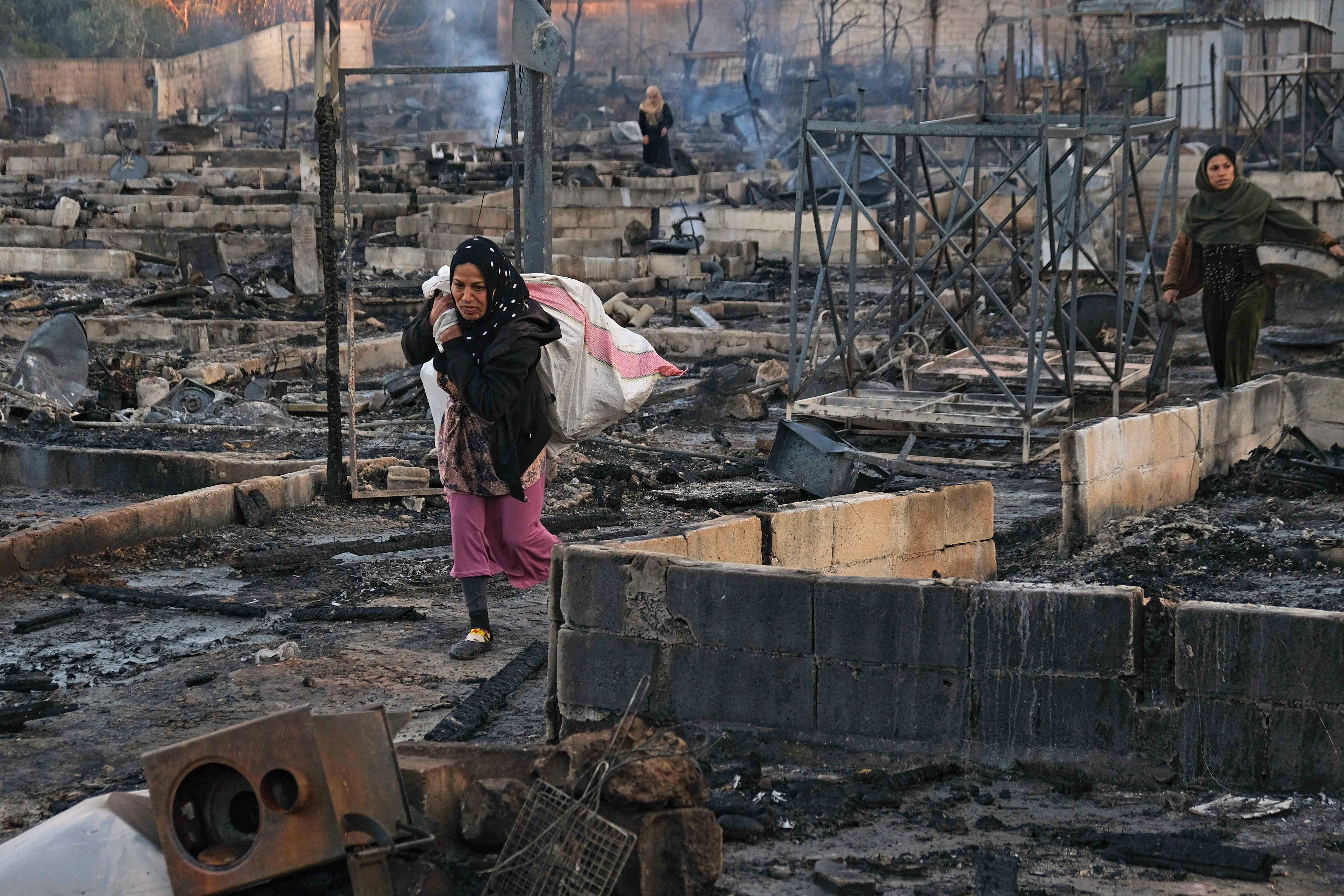 Syrian refugees salvage belongings from the wreckage of their shelters at a camp set on fire overnight in the northern Lebanese town of Bhanine on December 27, 2020 [File: Ibrahim Chaloub/AFP]