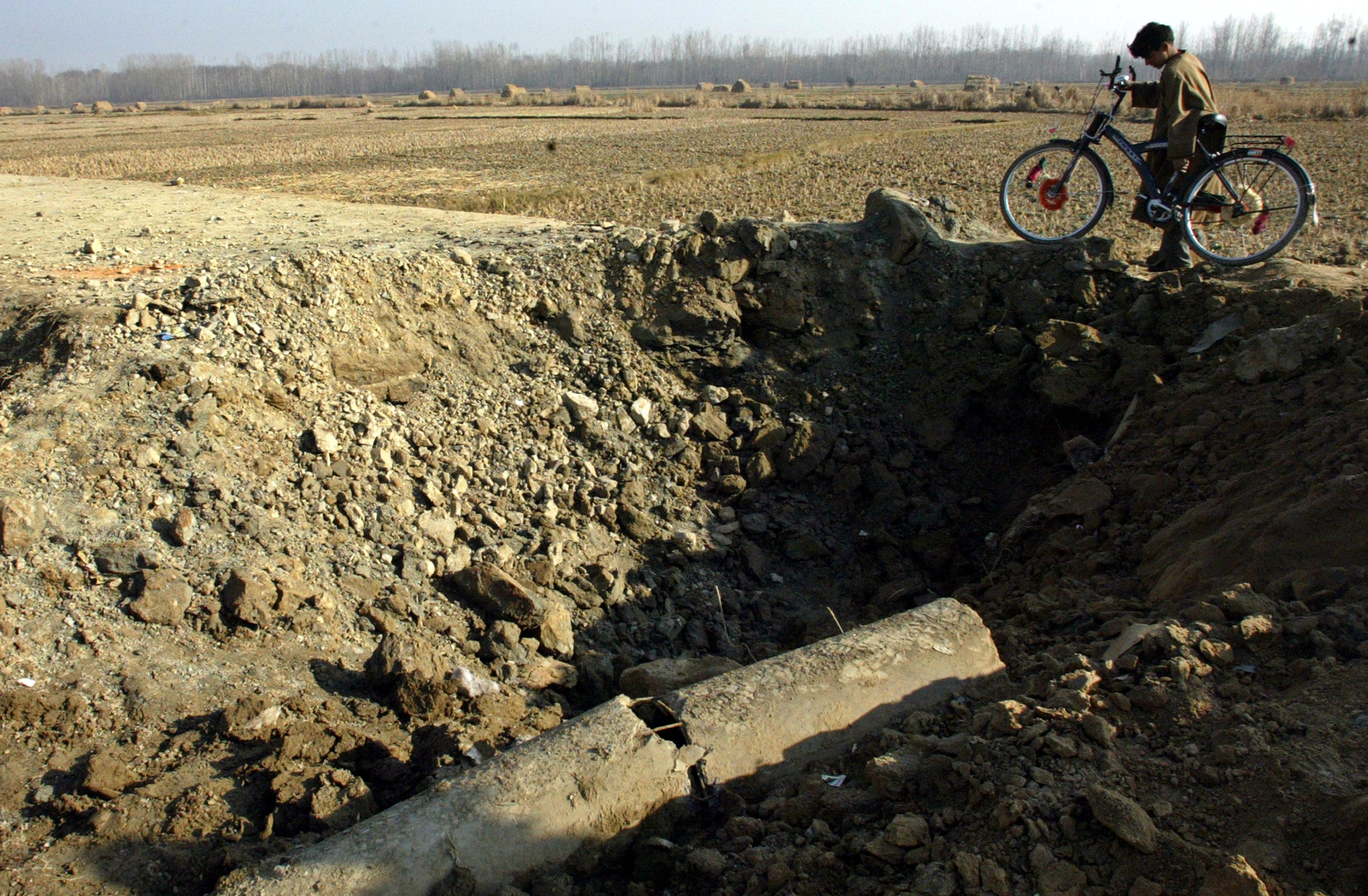 A Kashmiri boy with a bicycle walks past a crater caused by a landmine blast, in a photo from December 2004 [File: Reuters]