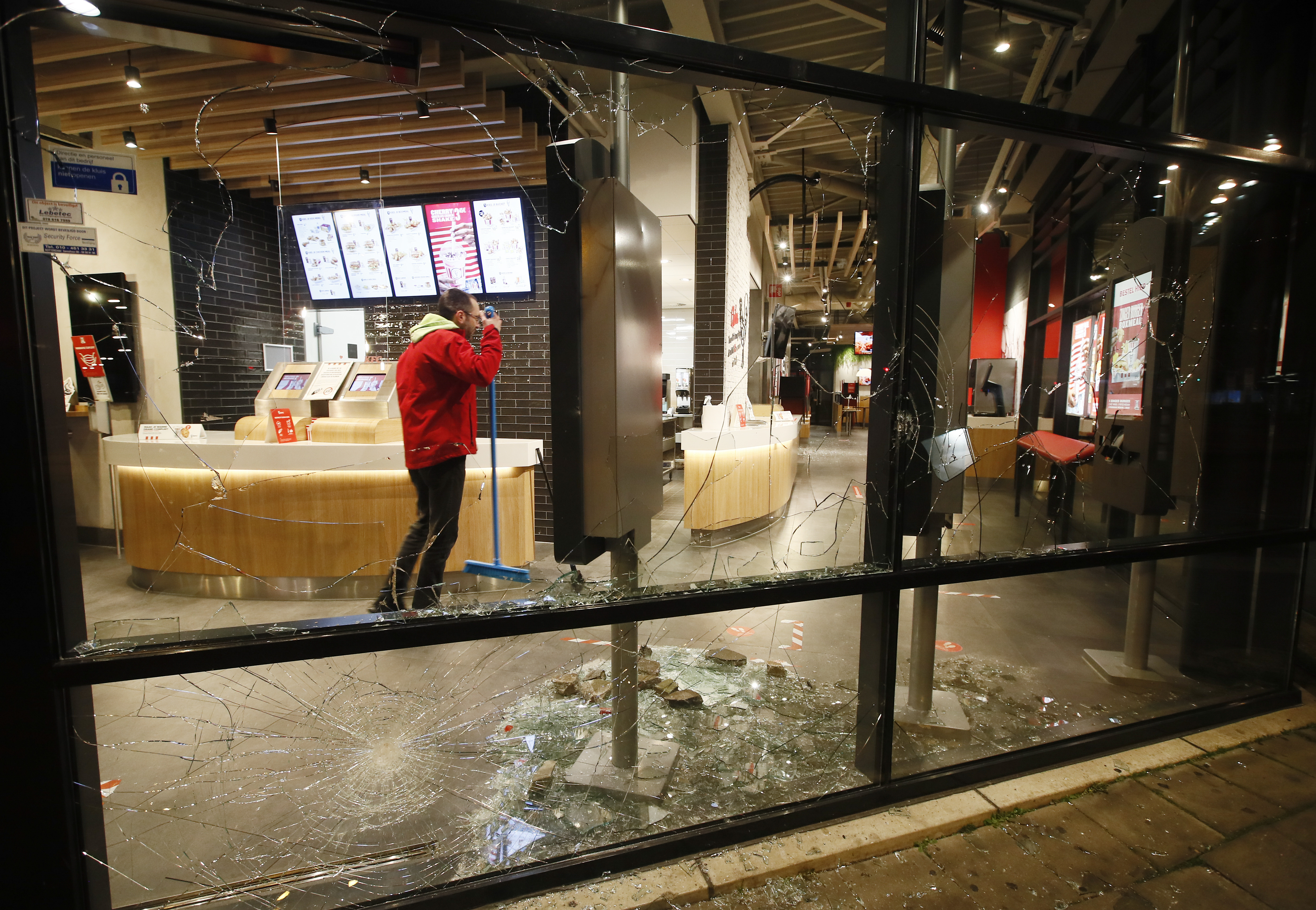 A man cleans up broken glass from the smashed windows in a fast-food restaurant that was damaged in protests against a nation-wide curfew in Rotterdam, Netherlands, Monday, January 25, 2021 [Peter Dejong/AP]