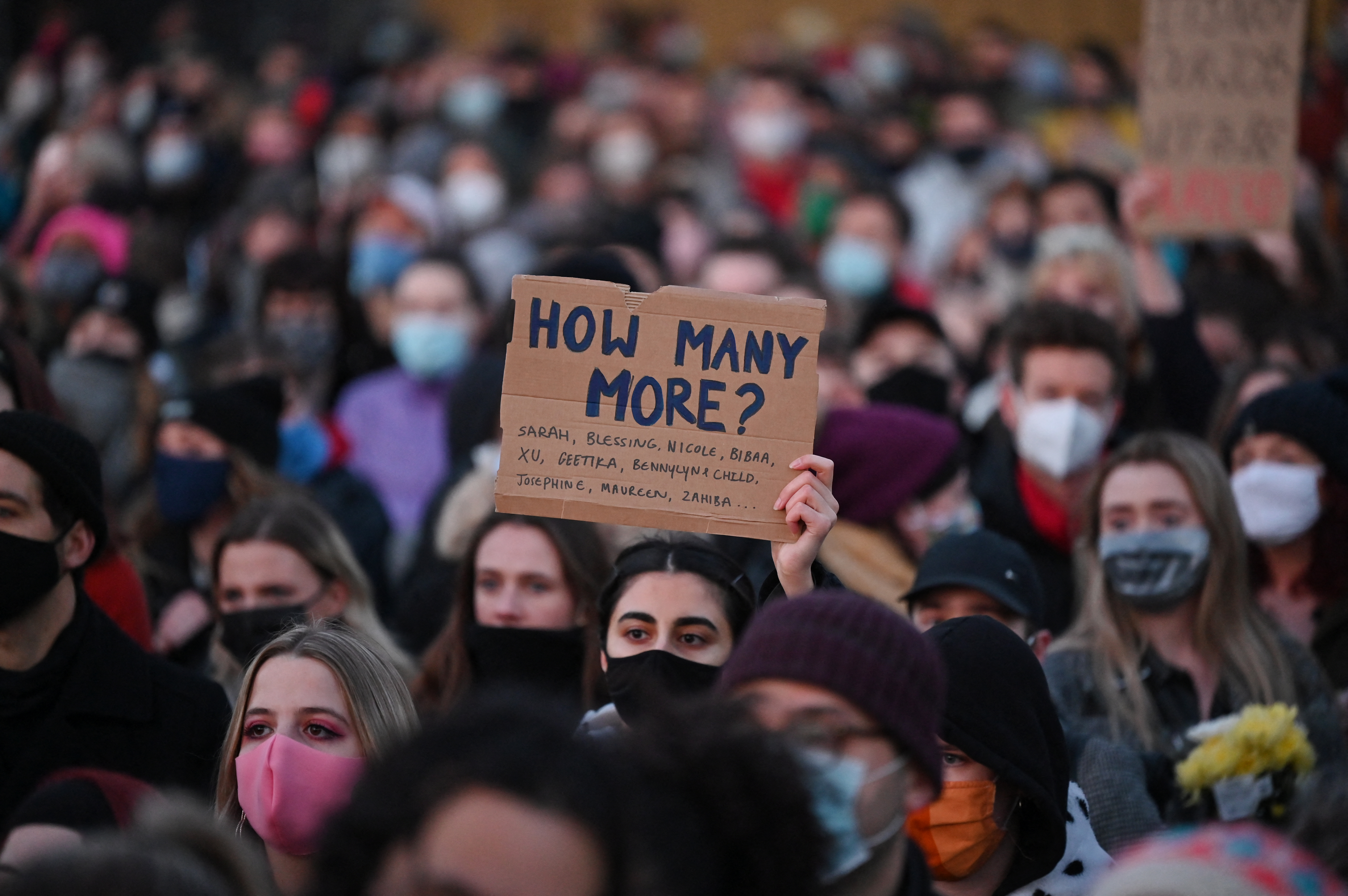 Well-wishers, one with a placard that reads 'How many more?', gather at a vigil in honour of murder victim Sarah Everard, in Clapham, south London, England on March 13, 2021 [Justin Tallis/AFP]