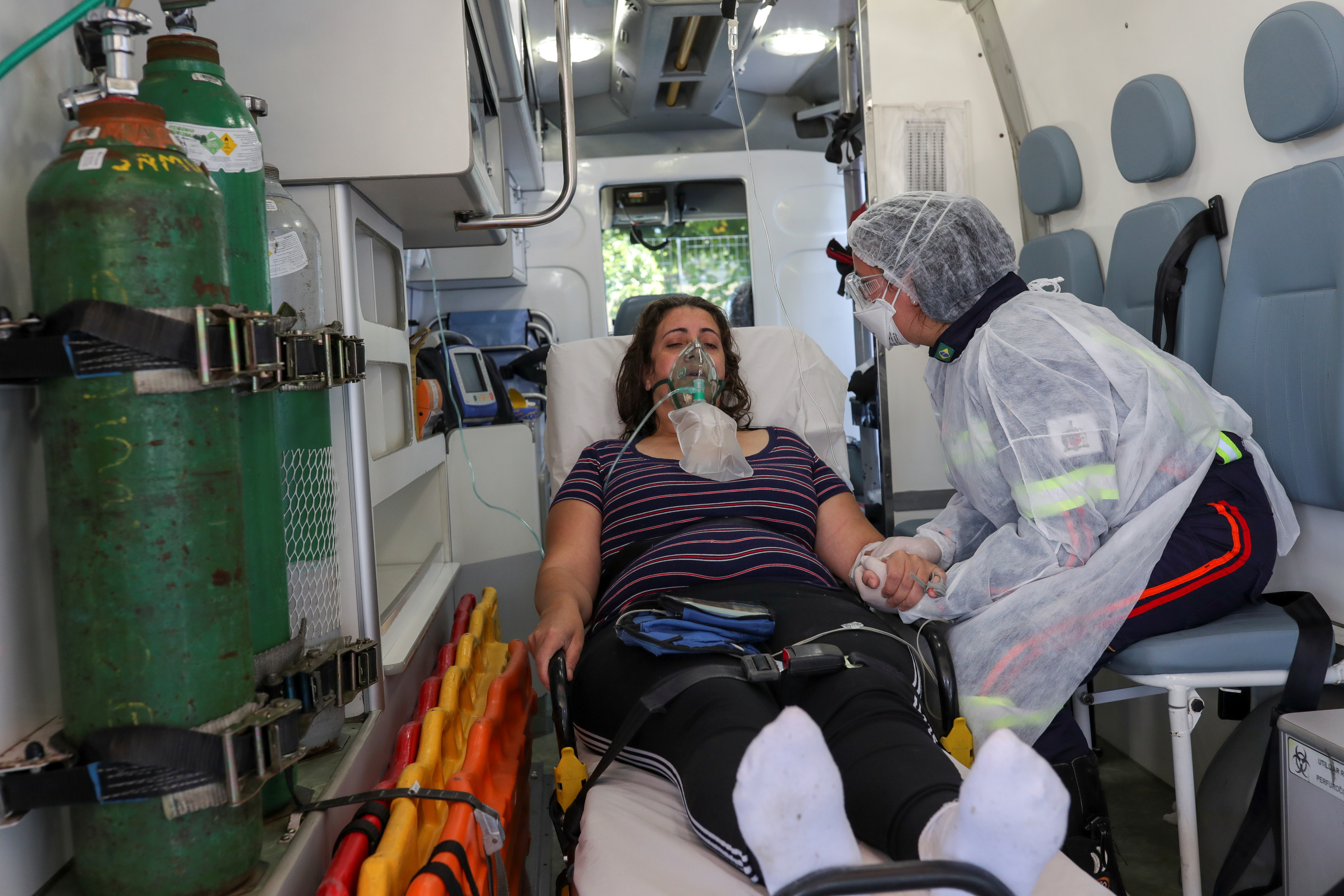 Nurse Danila Bassi holds the hand of Marley das Gracas, 42, who tested positive for COVID-19, inside an ambulance, in Sao Bernardo do Campo, Brazil, on March 24 [Amanda Perobelli/Reuters]