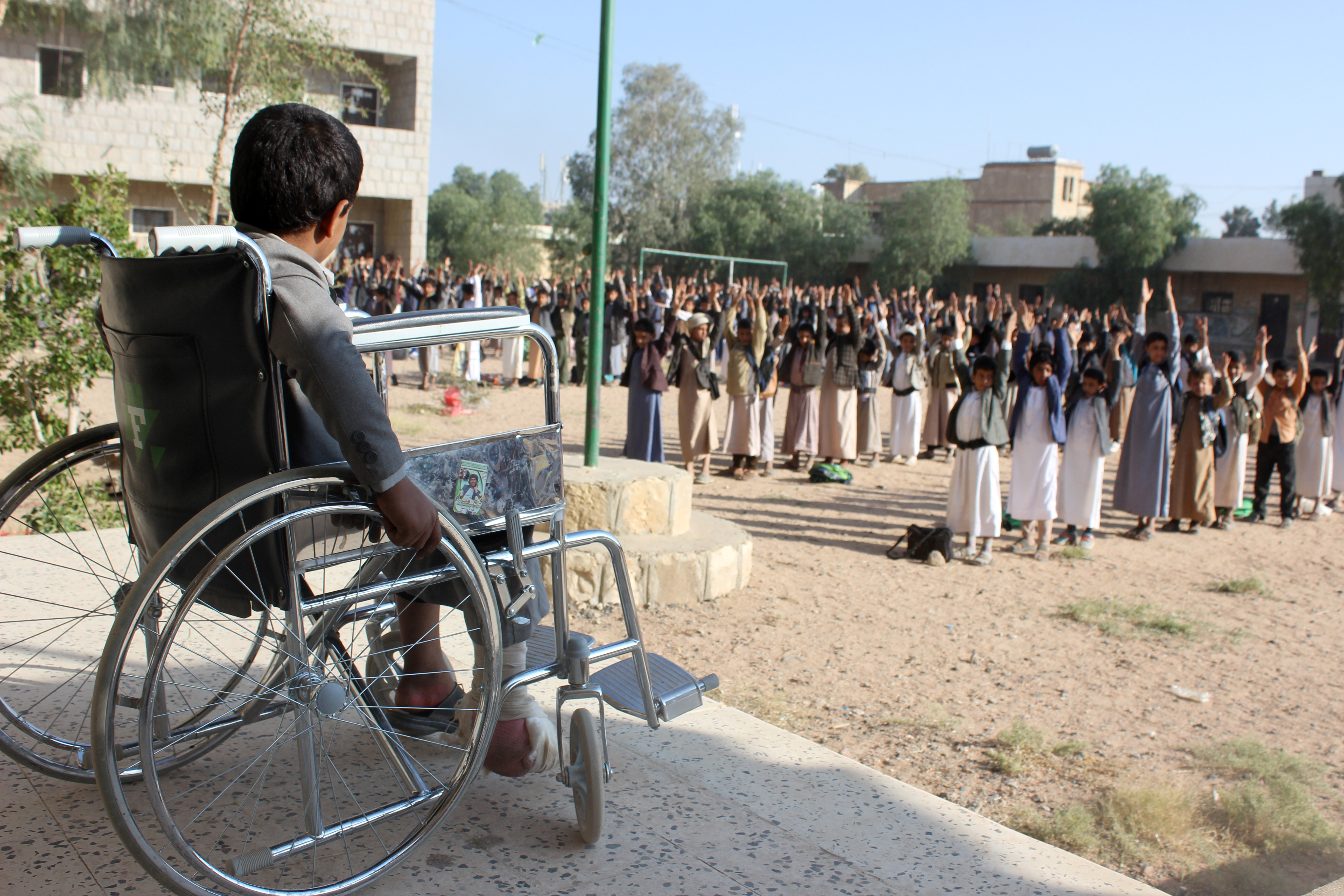 Muhammad al-Shadheli, nine, who survived an August 2018 Saudi-led air strike on a school bus, sits in a wheelchair during the morning drill at his school in Saada province, Yemen on October 6, 2018 [File: Reuters/Naif Rahma]