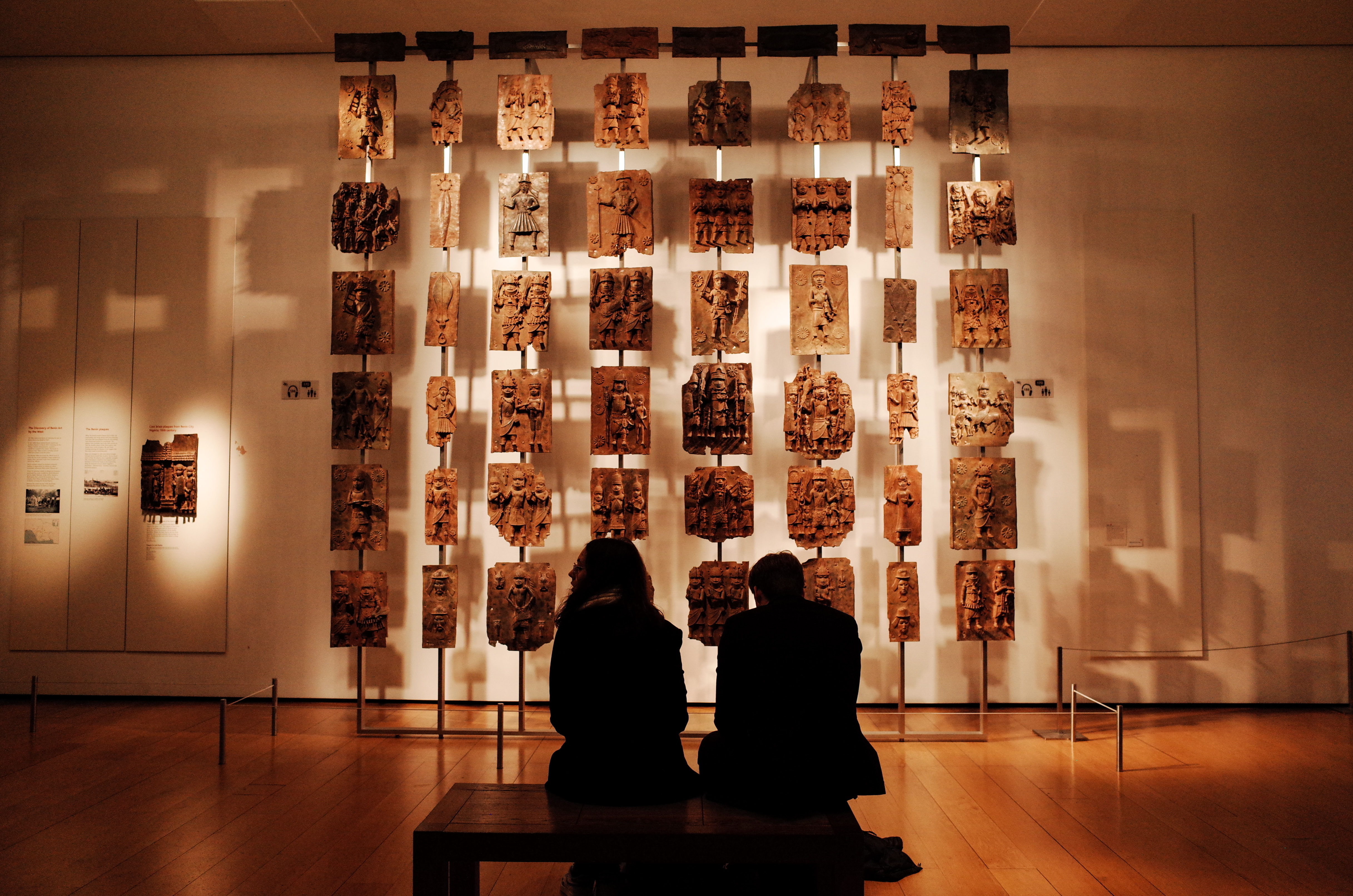 Visitors sit before the contentious Benin plaques exhibit (more commonly known as the Benin Bronzes) at the British Museum in London, UK [File: David Cliff/SOPA Images/LightRocket via Getty Images]