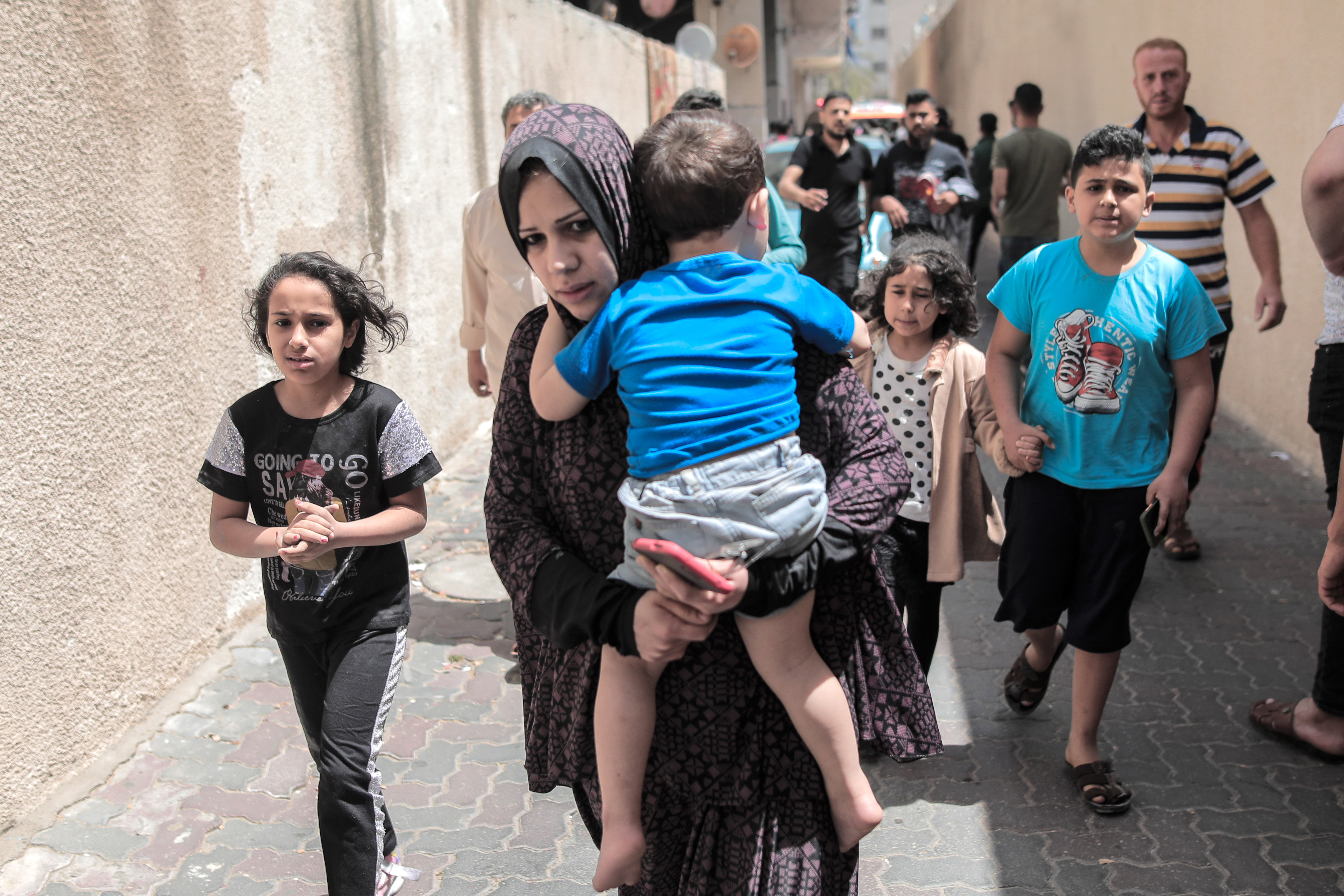 A mother carries her child in the street after the residential al-Jundi tower they live in was targeted by an Israeli drone in Gaza City [Hosam Salem/Al Jazeera]