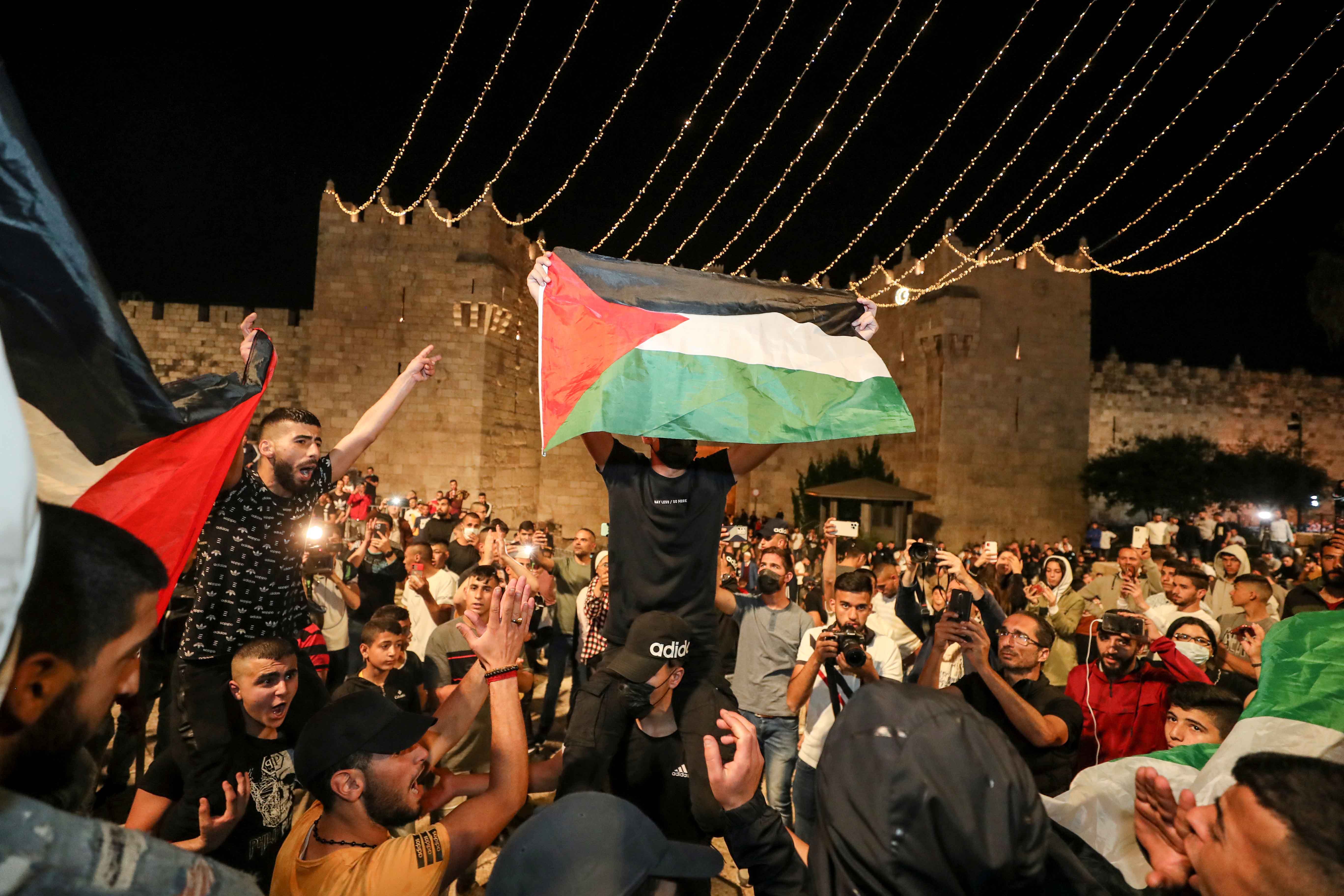 Palestinians wave flags and celebrate outside Damascus Gate on April 25, 2021, after barriers put up by Israeli police were removed, allowing them to access the main square that has been the focus of a week of clashes around Jerusalem's Old City [Reuters/Ammar Awad]