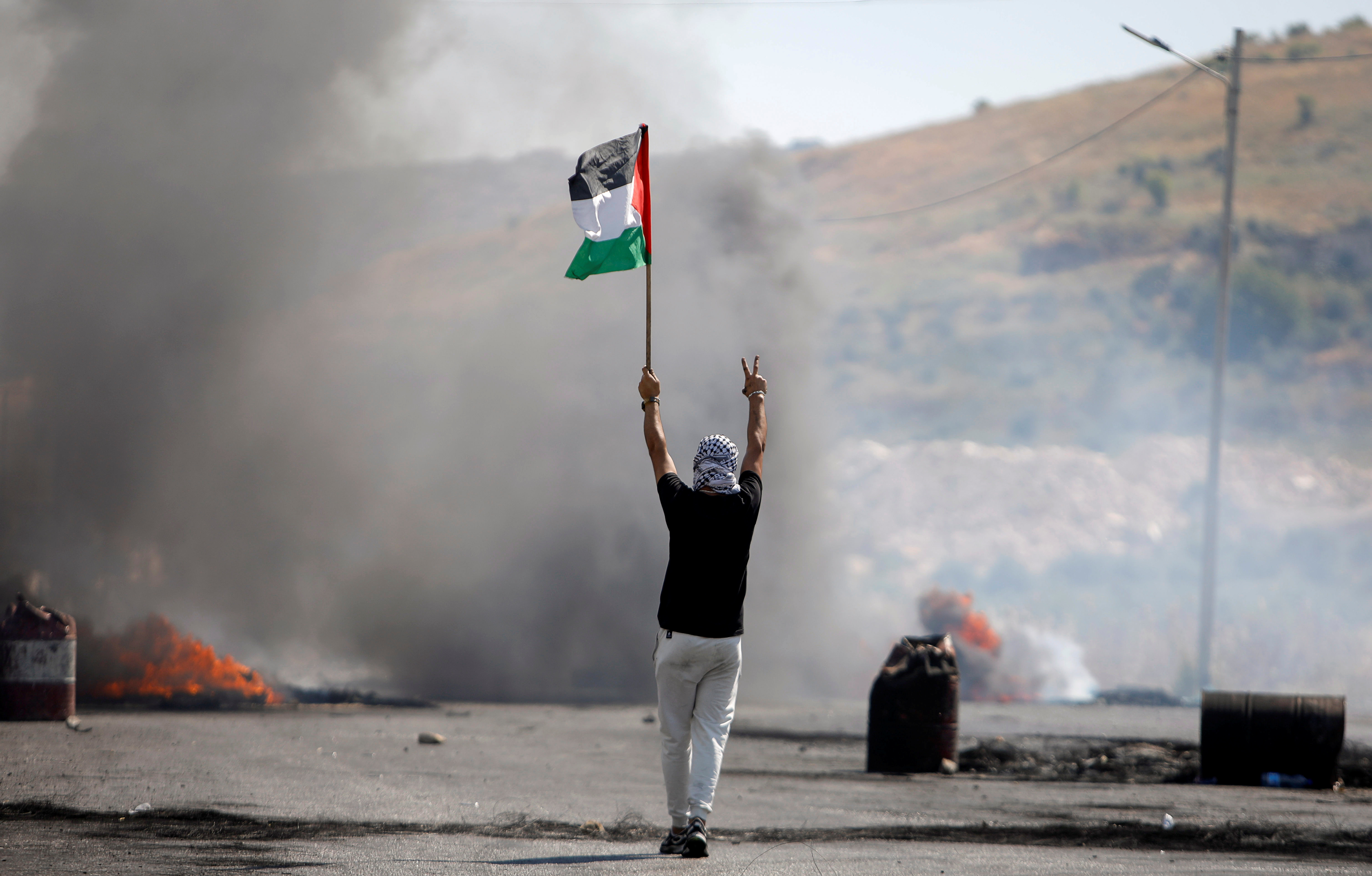 A demonstrator holding a Palestinian flag gestures during a protest, near Hawara checkpoint in the occupied West Bank, May 14, 2021 [File: Raneen Sawafta/Reuters]