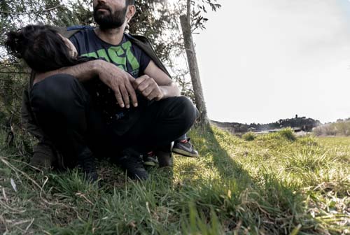 An Afghan man with a child waits in northwest Bosnia with a group of others, who are all trying to reunite with family members over the border in Croatia [Mana Sadeghi/Al Jazeera]