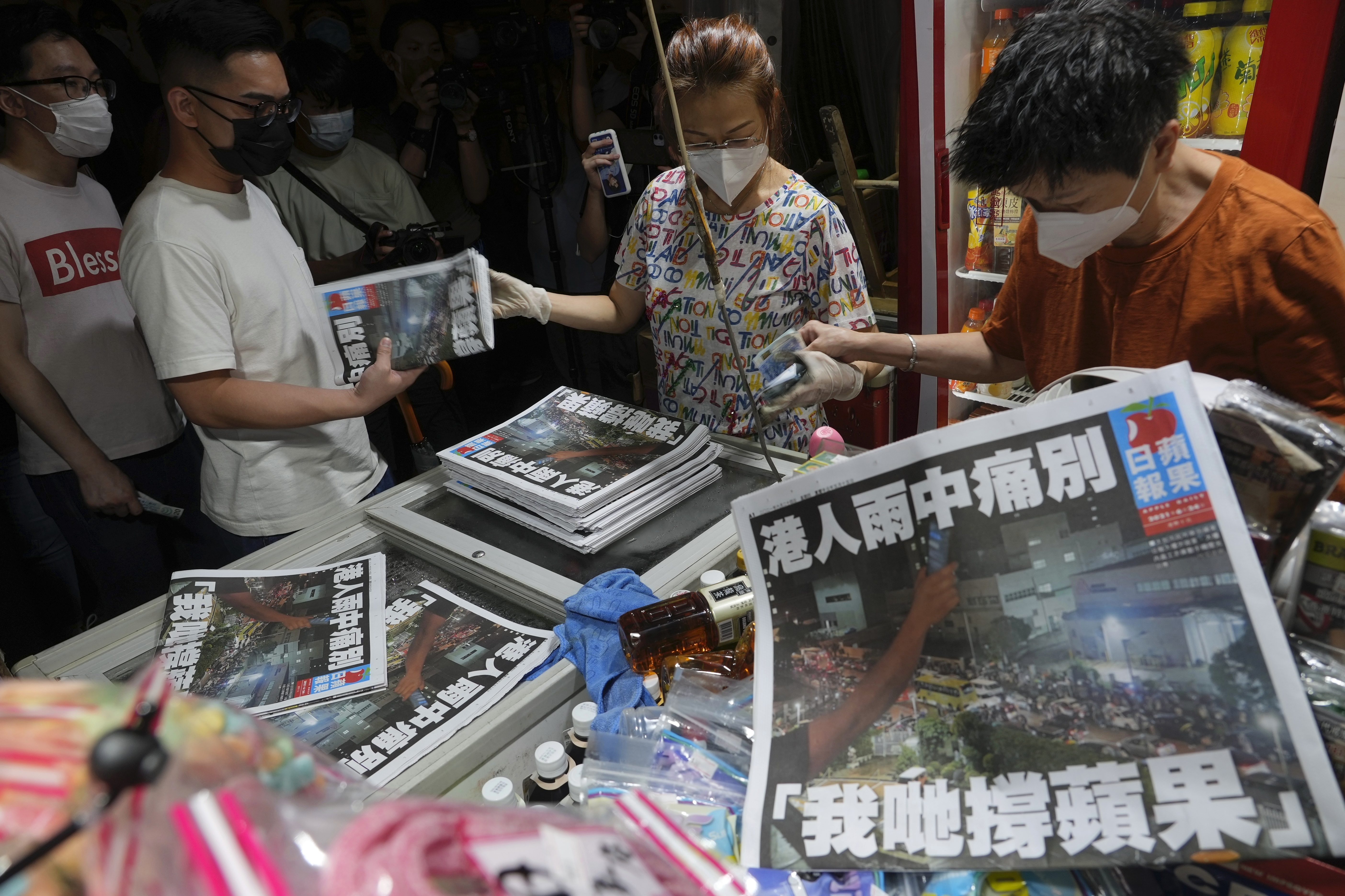 A woman hands out final editions of the Apple Daily as people queue to buy it. 