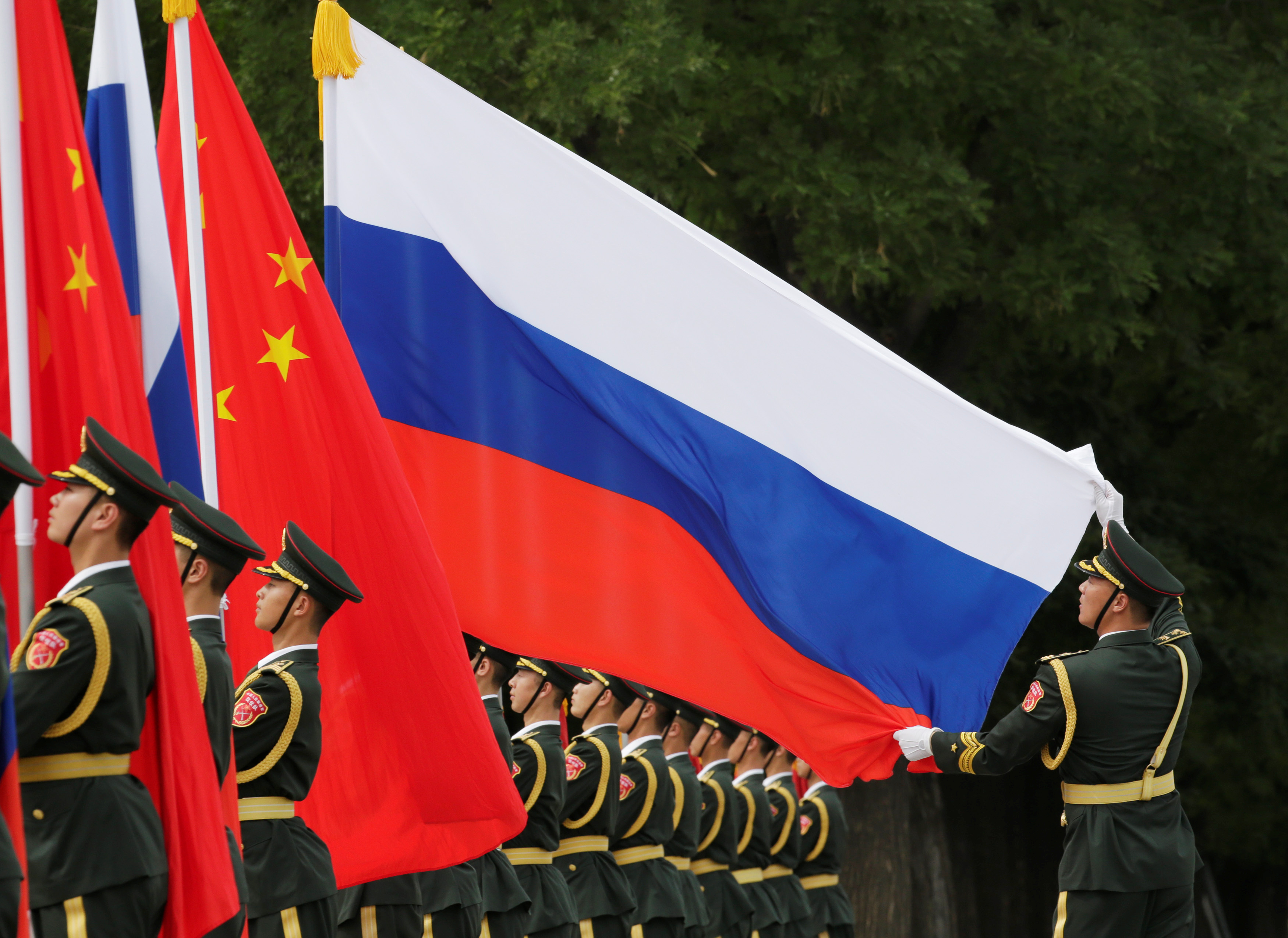 A military officer adjusts a Russian flag ahead of a welcome ceremony hosted by Chinese President Xi Jinping