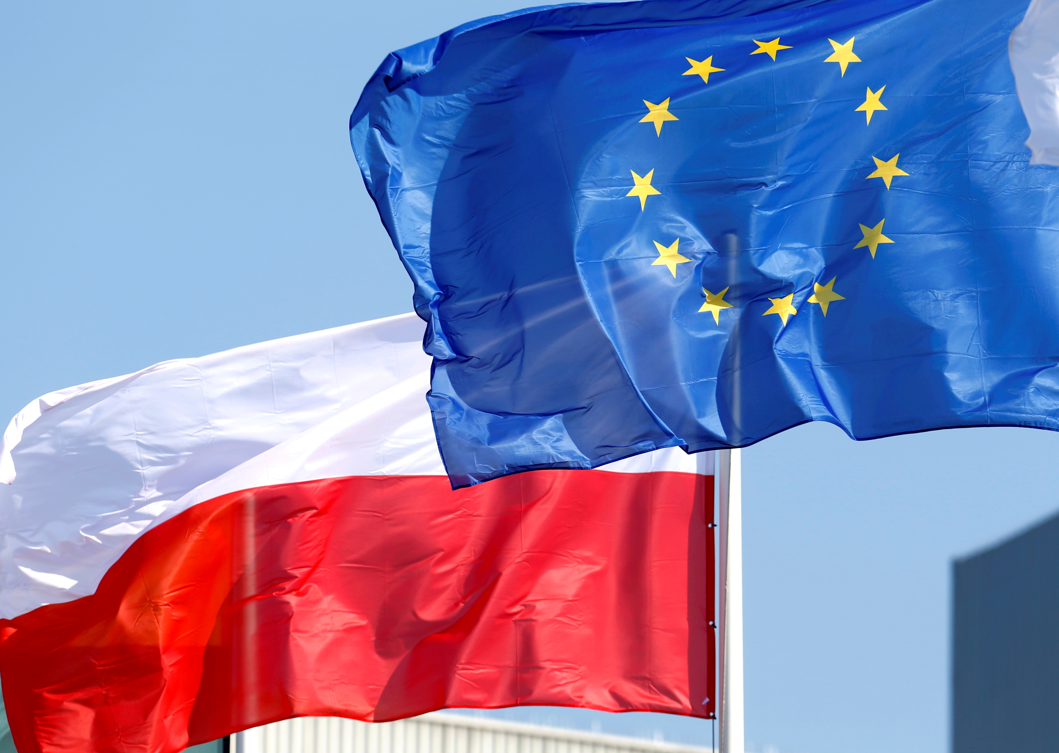 The Polish flag waves behind the EU flag.