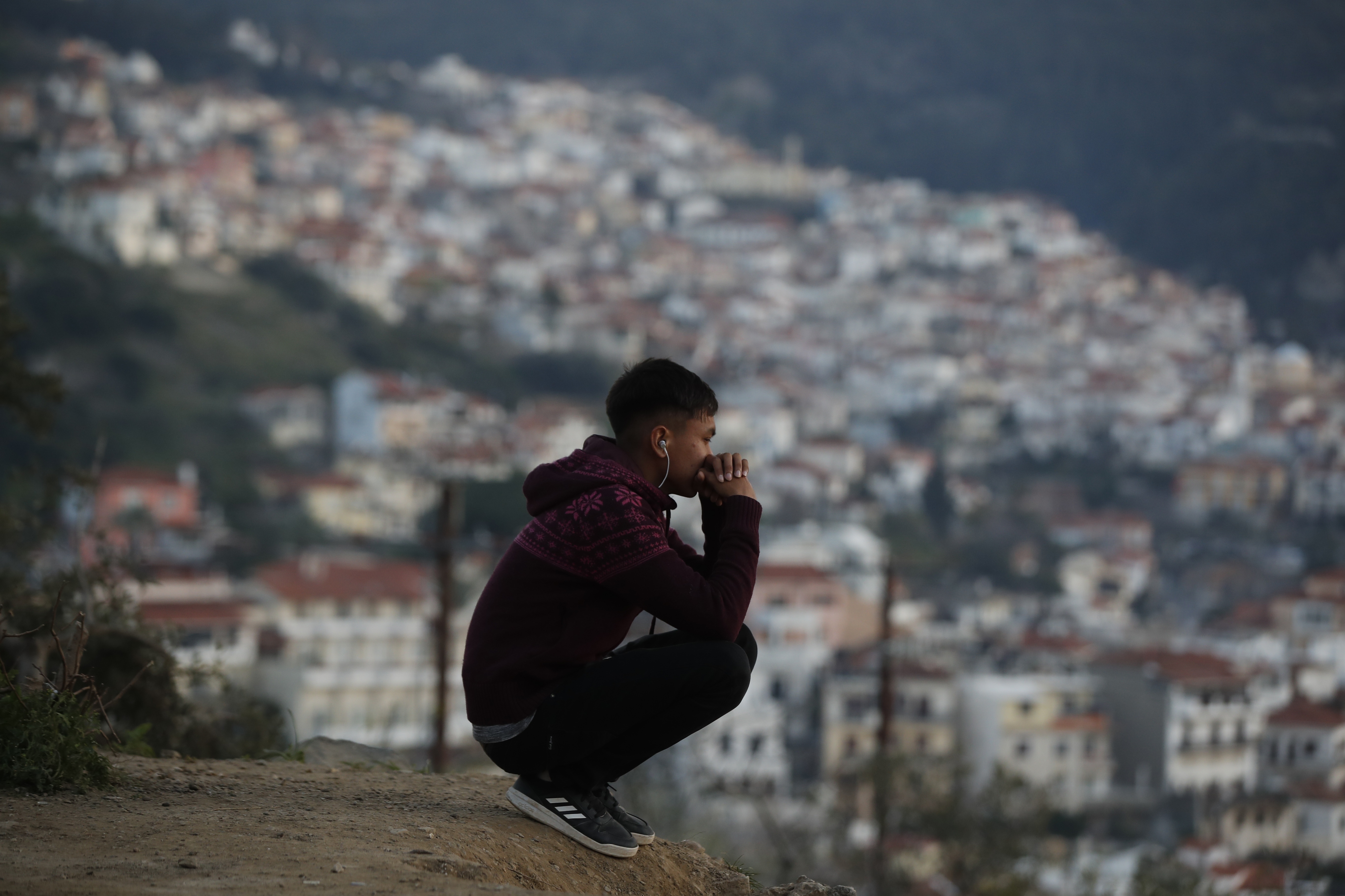 An asylum seeker sits on a hill outside the perimeter of the overcrowded refugee camp at Vathy on the eastern Aegean island of Samos, Greece, on February 23, 2021 [File: Thanassis Stavrakis/AP]