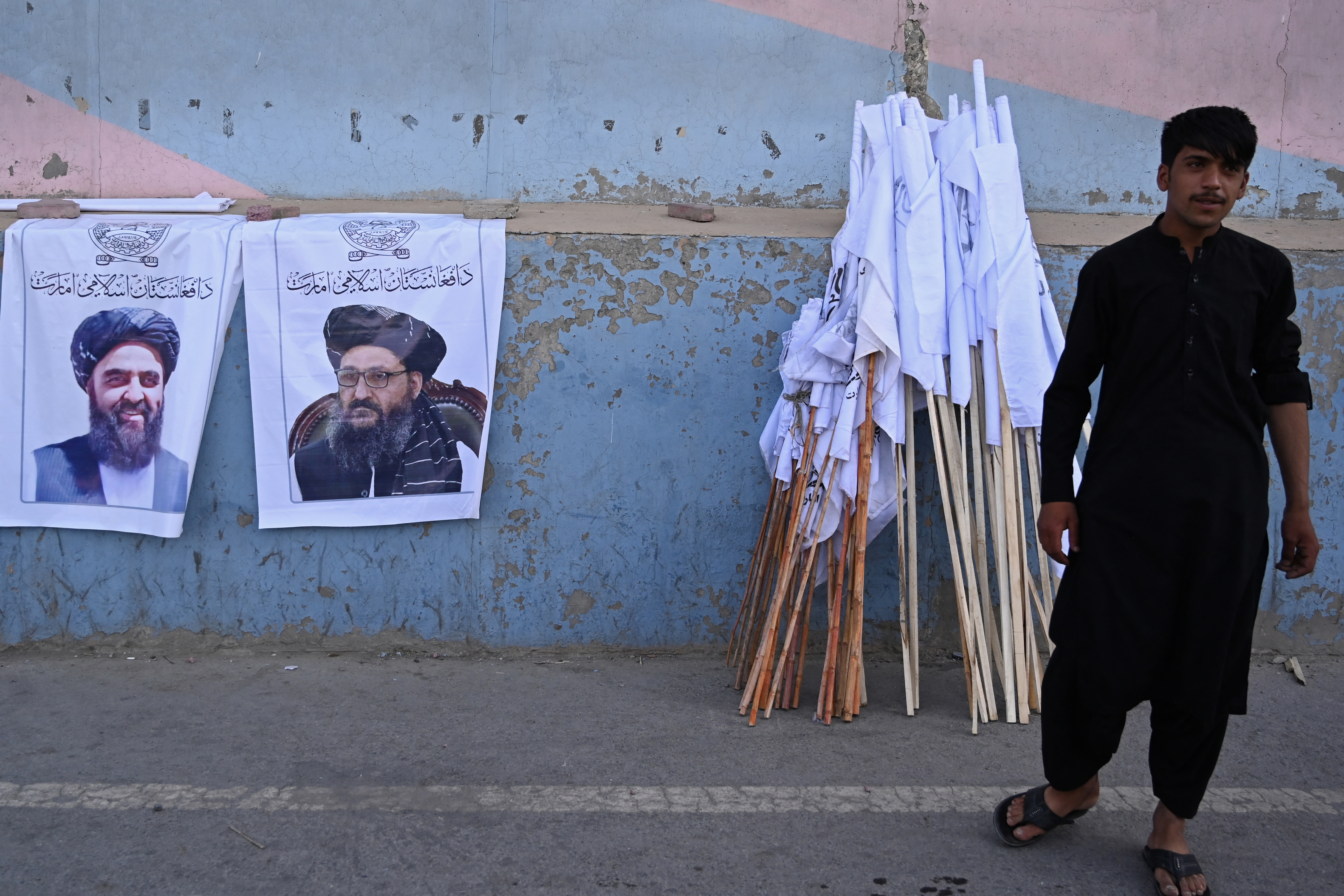 A vendor selling Taliban flags stands next to posters of Taliban leaders Mullah Abdul Ghani Baradar and Amir Khan Muttaqi (L) as he waits for customers along a street in Kabul on August 27, 2021. [Aamir Qureshi/ AFP]