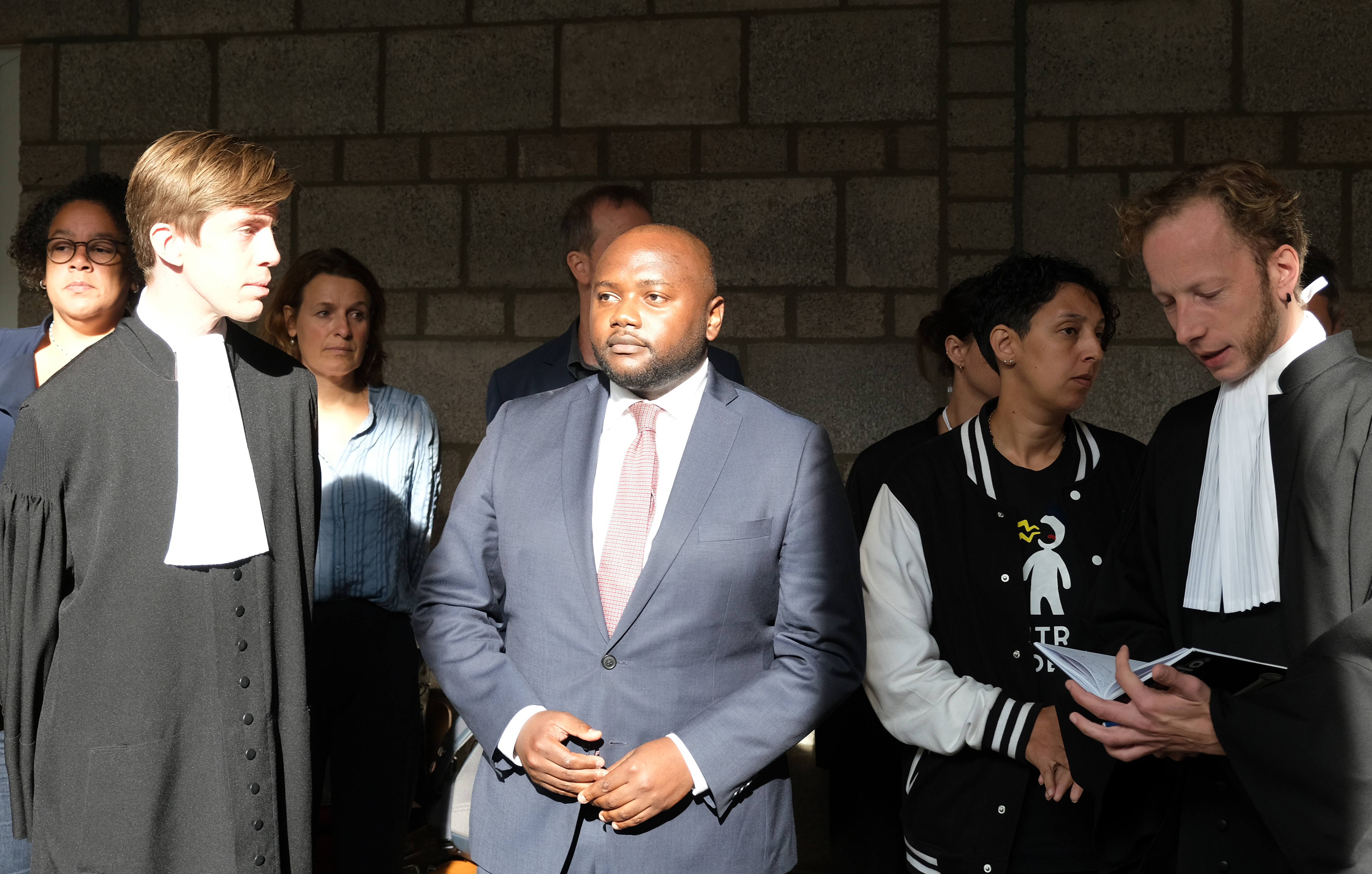 Mpanzu Bamenga, centre, stands with his legal team and rights activists outside a courtroom at The Hague District court, Netherlands, Wednesday September 22, 2021, after losing a case. A Dutch court ruled that border police can use ethnicity as one of the criteria for selecting people for checks at the border, a legal defeat equal rights activists immediately vowed to appeal [AP Photo/Mike Corder]