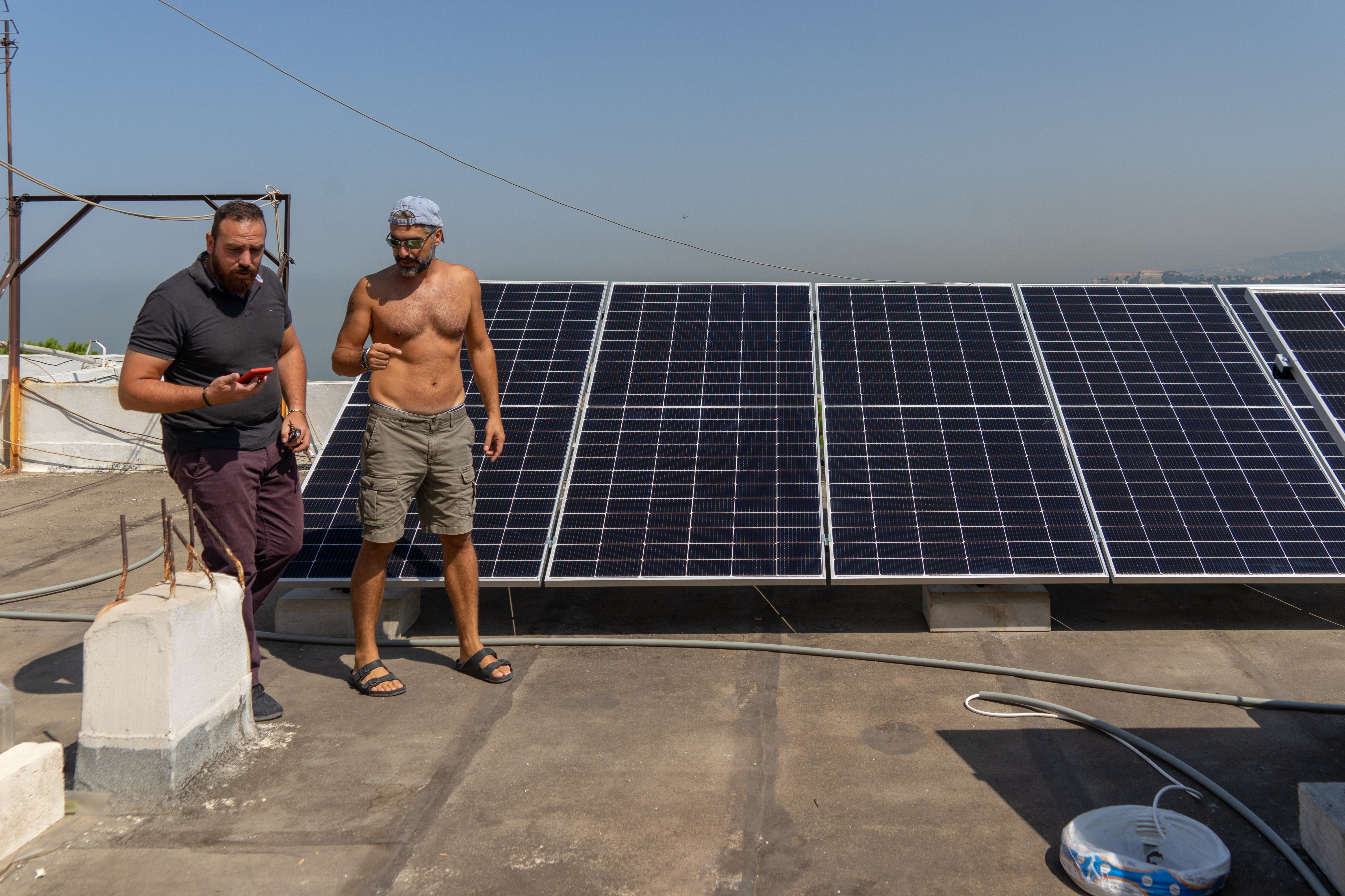Contractor Chawki Lahoud, left, updates Samer Maatouk on the solar power system he installed for him in front of photovoltaic solar panels in Broummana, Lebanon [Adam Muro/Al Jazeera]