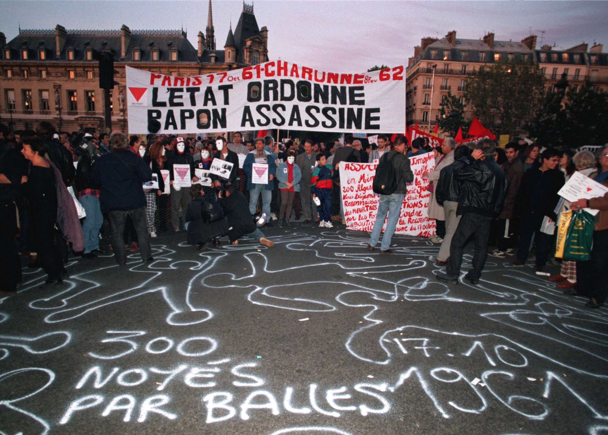 At a 1997 protest, people hold a banner reading 'The State Orders - Papon Assassinates' in front of an inscription on the pavement, '300 drowned by bullets' [File: Reuters]